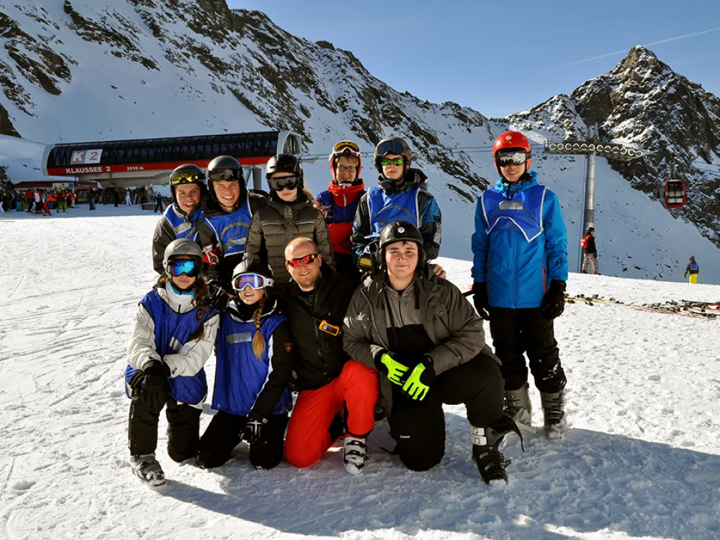 Skigruppe posiert vor der Bergstation und den Felsgipfeln.